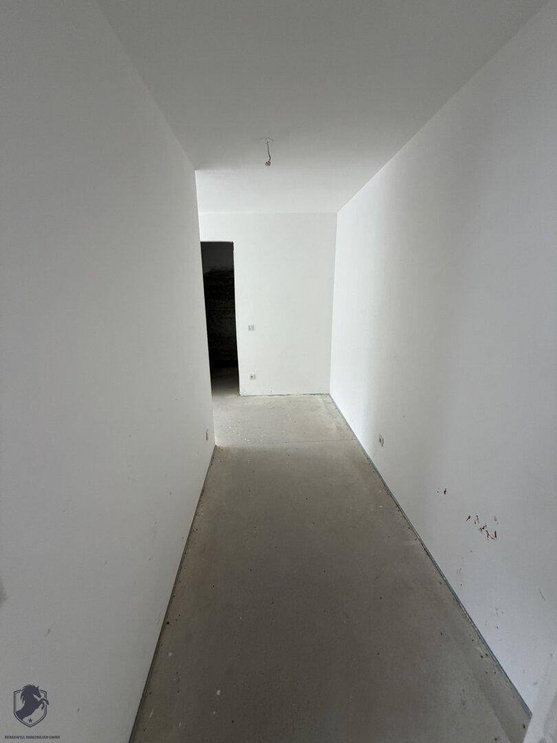 Leerer Flur im Rohbau mit glattem Betonboden und weißen Wänden, bereit für den Ausbau.
