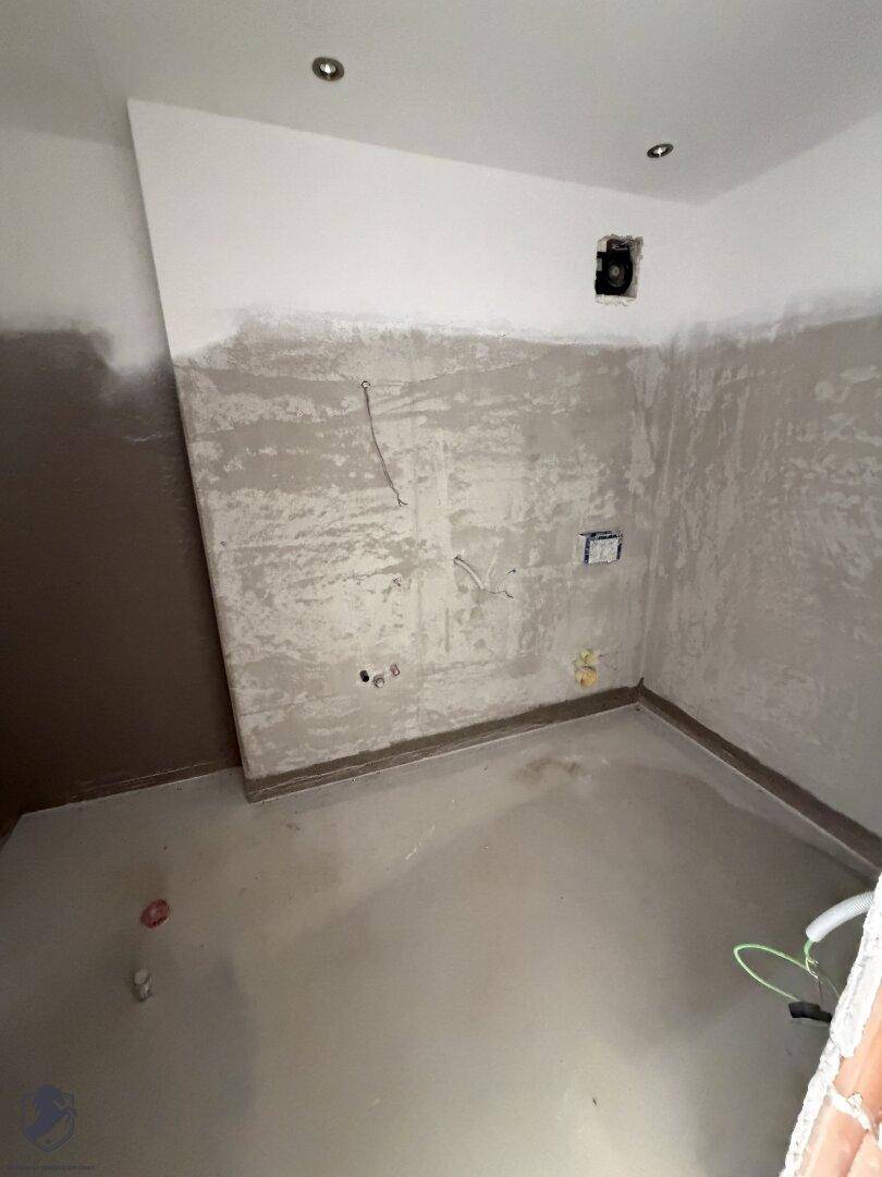 Rohbau-Raum mit sichtbaren Leitungen und vorbereiteten Wänden, ideal für eine zukünftige Küche oder Bad.
