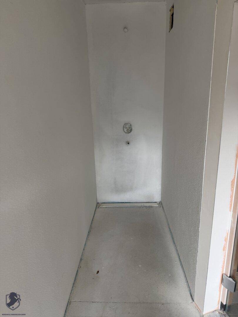 Duschbereich im Rohbau mit vorbereitetem Abfluss und Wänden, bereit für die Fliesenverlegung.
