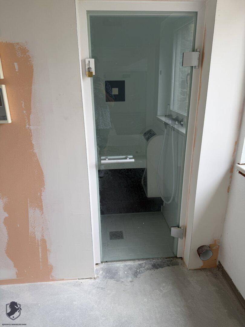 Eingang zu einer modernen Dampfdusche mit Glastür und minimalistischer Ausstattung.