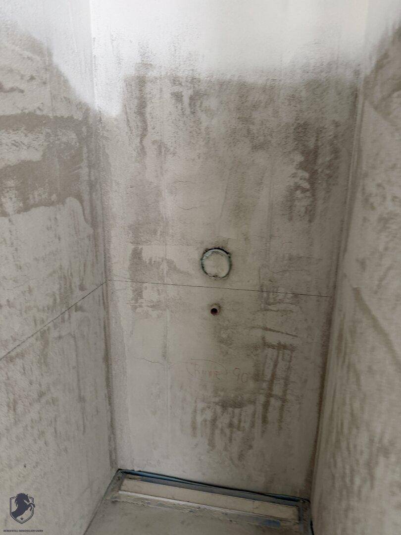 Detailansicht eines Duschbereichs im Rohbau mit Betonwänden und vorbereitetem Bodenablauf.