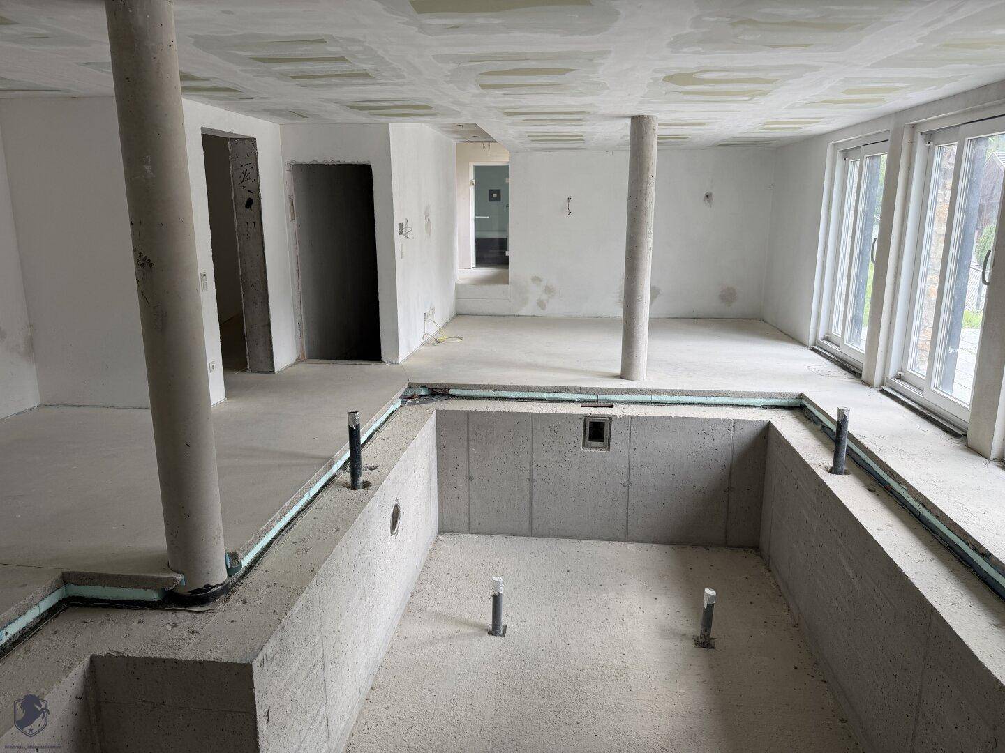 Offener Rohbau mit einem großen Poolbecken, Säulen und einer Fensterfront für viel Helligkeit.