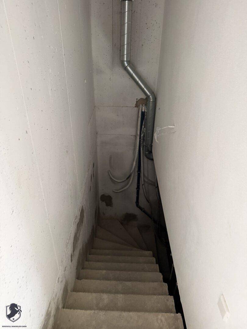 Betontreppe führt in den Kellerbereich, umgeben von unverputzten Wänden und sichtbaren Leitungen.