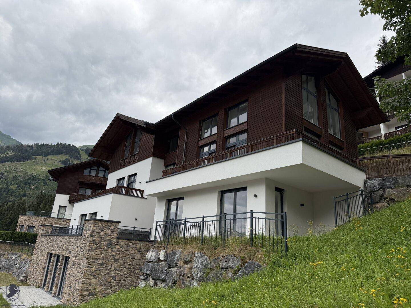 Moderne Architektur mit Holz- und Weißfassaden, Steinverkleidung und Balkonen in alpiner Landschaft.