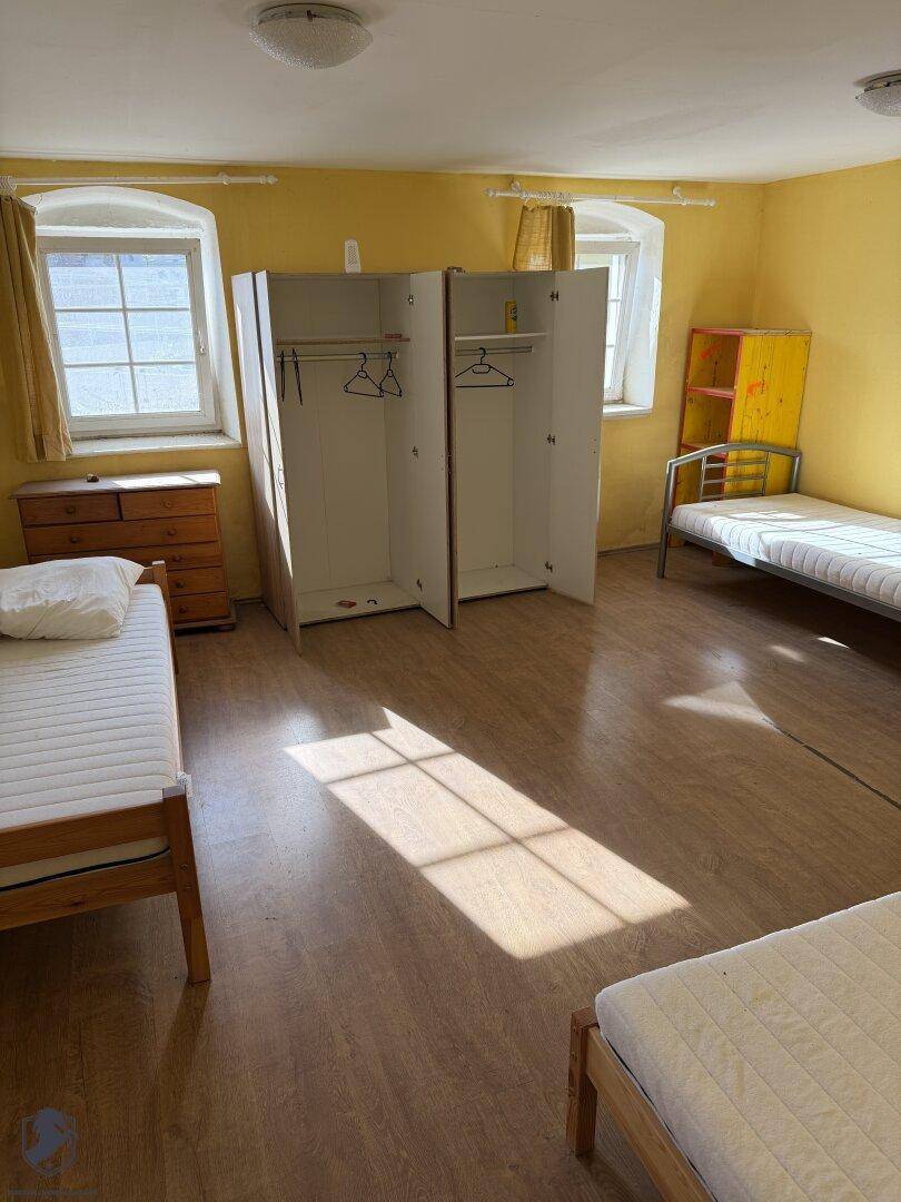 Helles Schlafzimmer mit mehreren Betten, Holzfußboden und gelben Wänden.