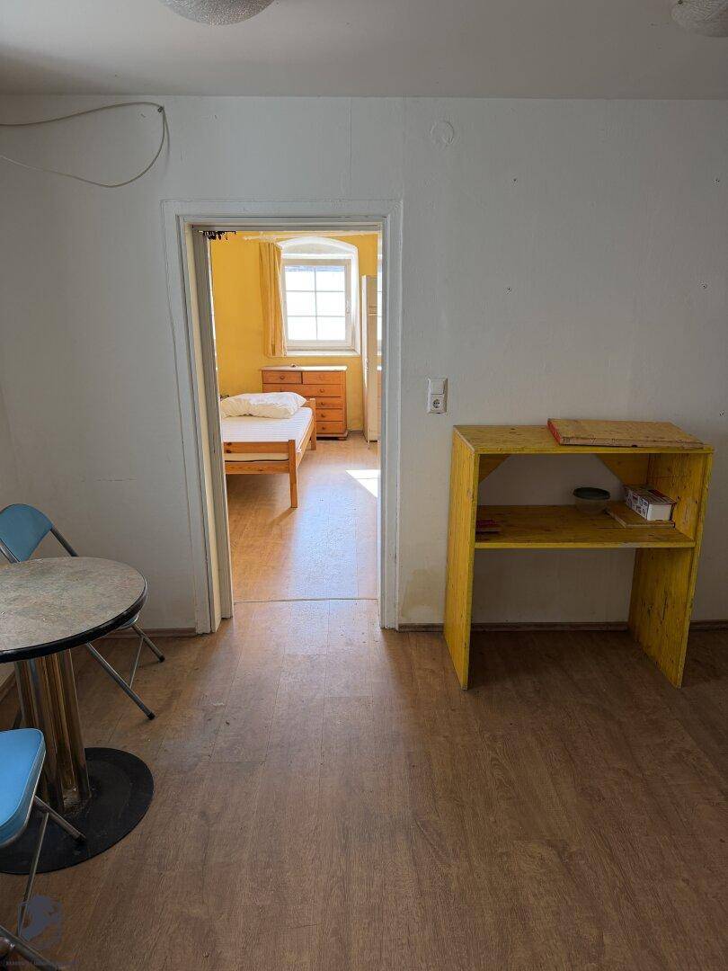 Durchgangsbereich mit Holzboden, der zu einem hellen Schlafzimmer mit gelben Wänden führt.
