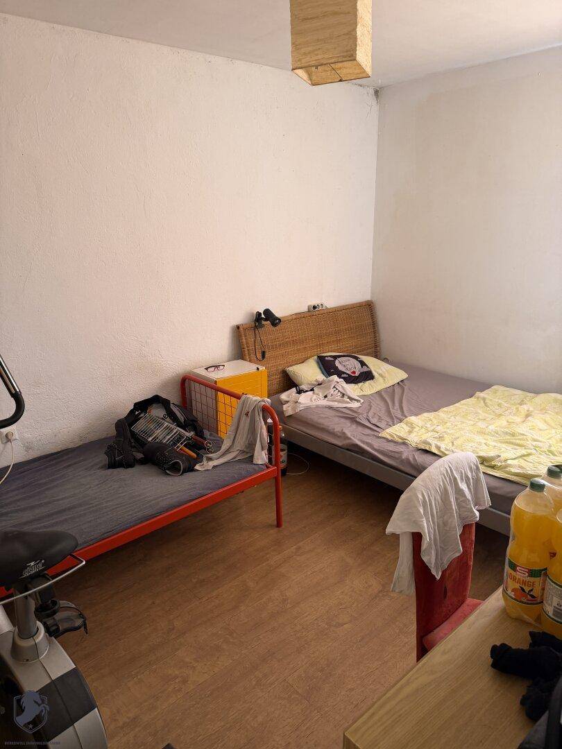 Einfaches Schlafzimmer mit zwei Betten, Holzboden und weiß gestrichenen Wänden.