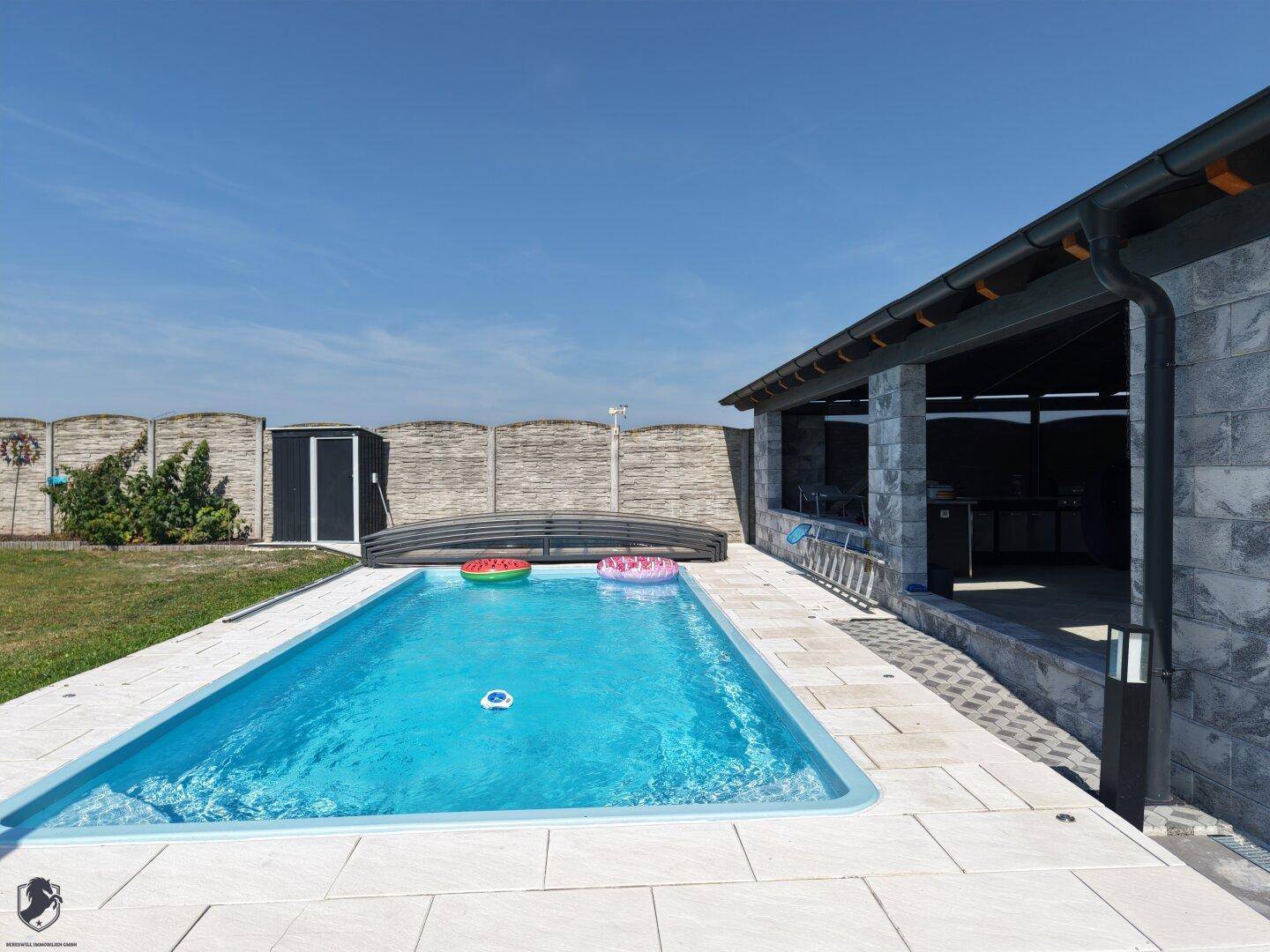 Detailansicht des Pools mit Liegeflächen und der angrenzenden überdachten Terrasse.