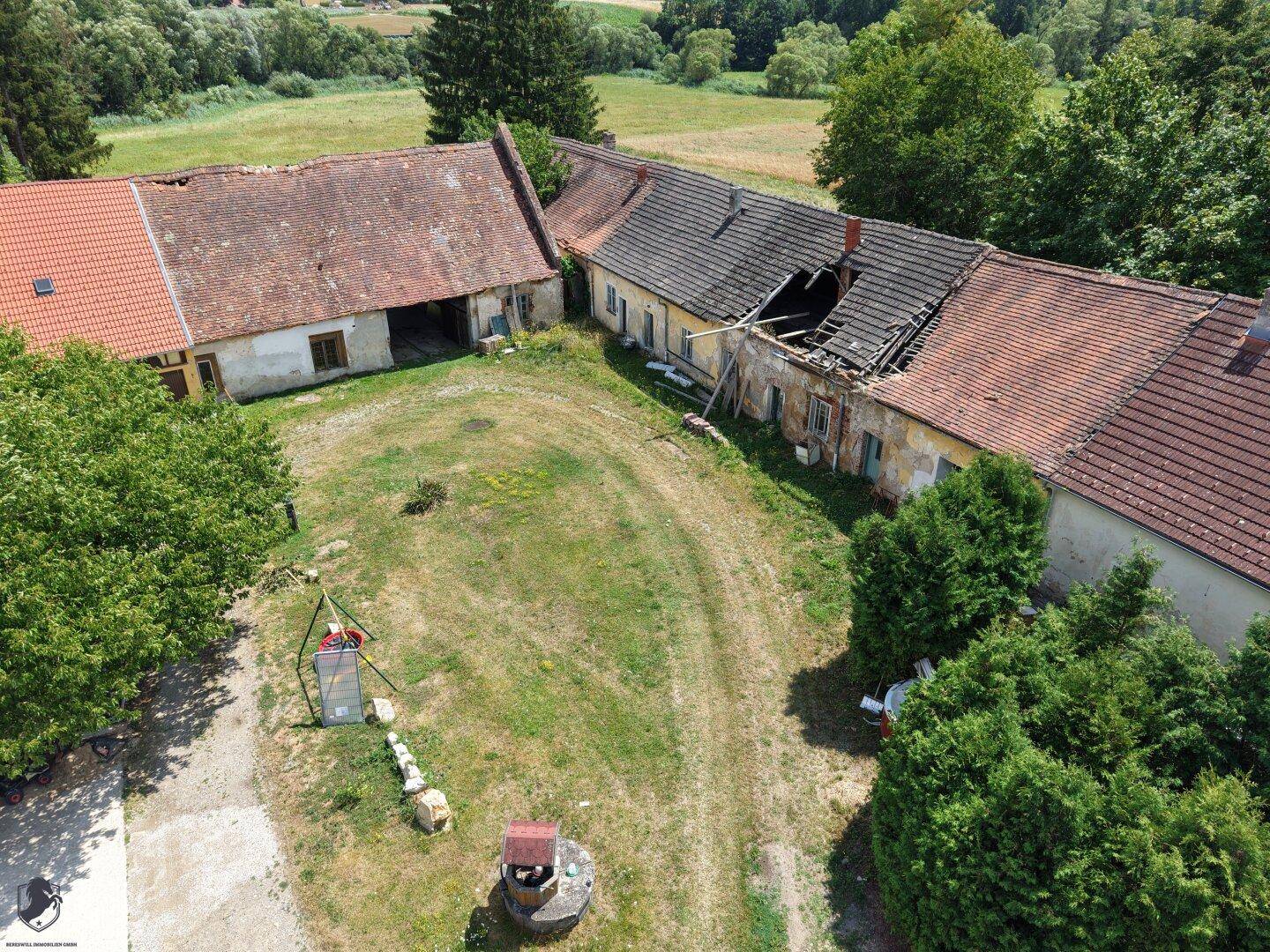 Blick auf einen großen Innenhof mit Brunnen und teilweise verfallenen Gebäuden des Anwesens.