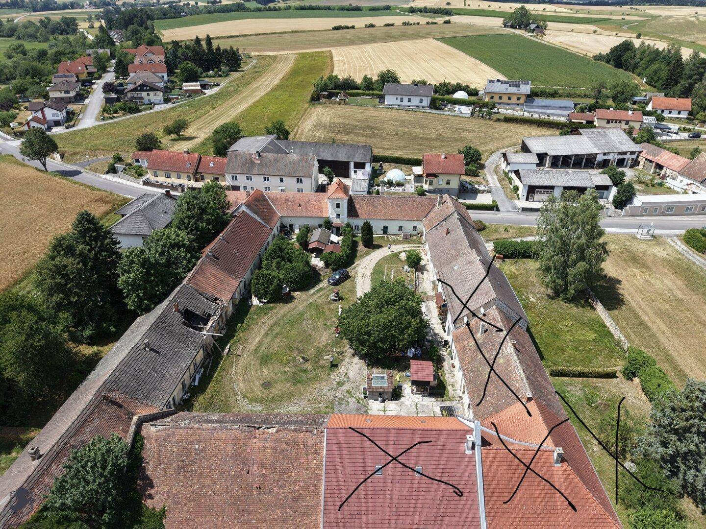Luftaufnahme des weitläufigen Anwesens mit mehreren Gebäuden und umliegenden Feldern aus der Vogelperspektive.