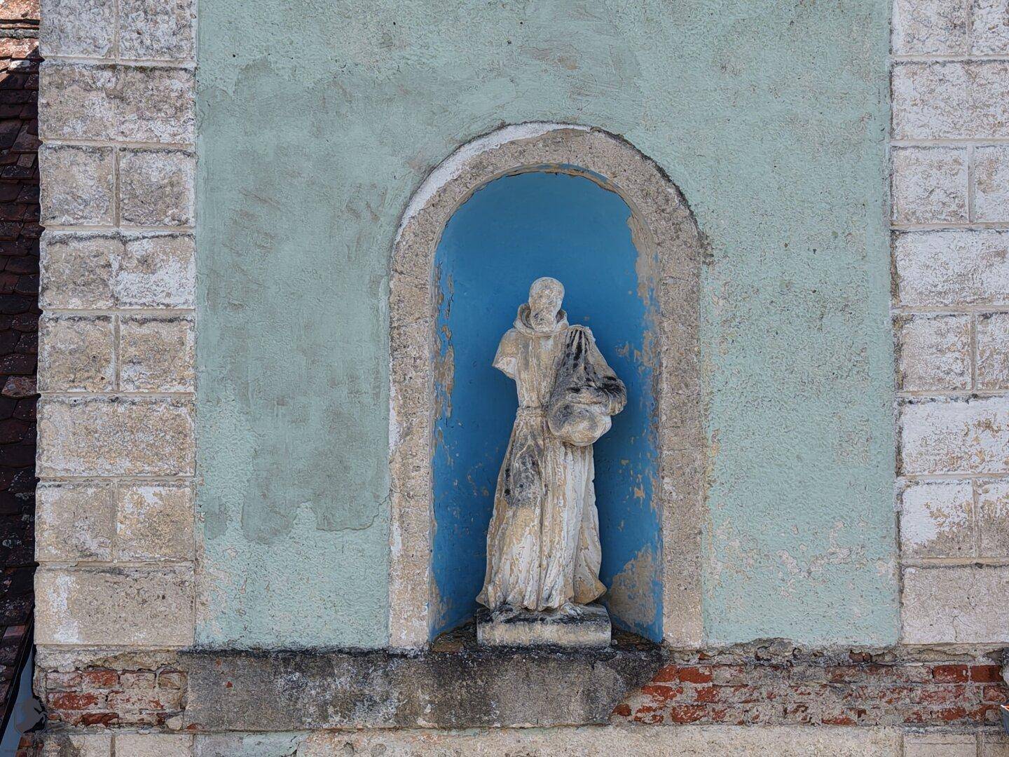 Historische Nische in einer alten Mauer mit einer Statue, umgeben von verwittertem Putz und Ziegeln.