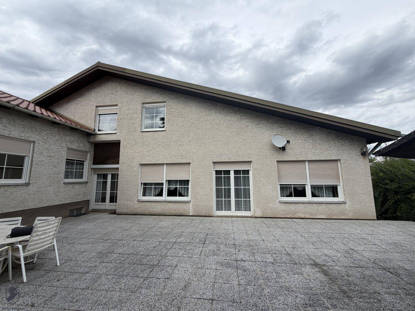 Fassade des Hauses mit großen Fenstern und einer geräumigen, gepflasterten Terrasse.