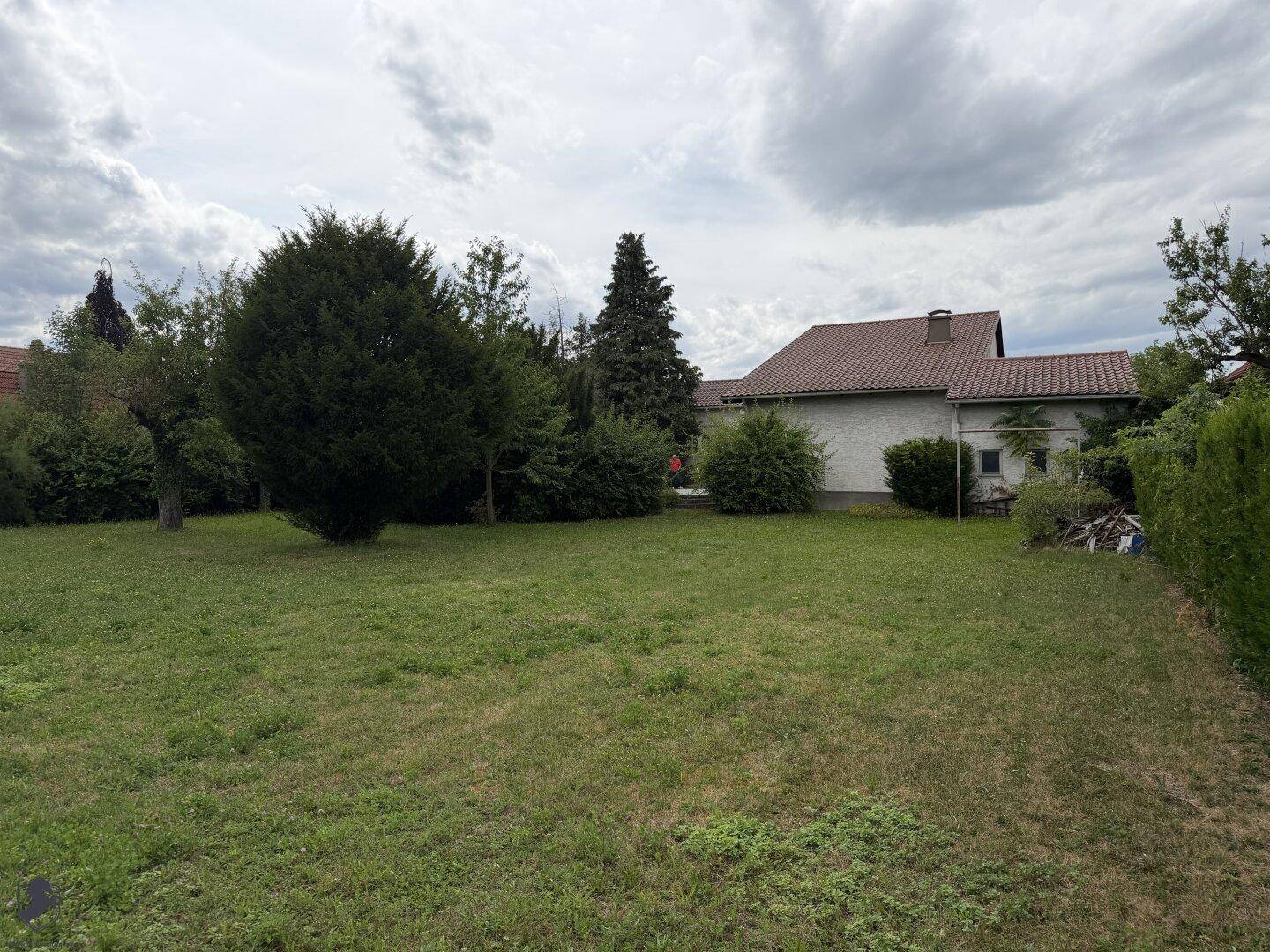 Weitläufiger Garten mit Rasenfläche und Bäumen, das Haus ist im Hintergrund zu sehen.