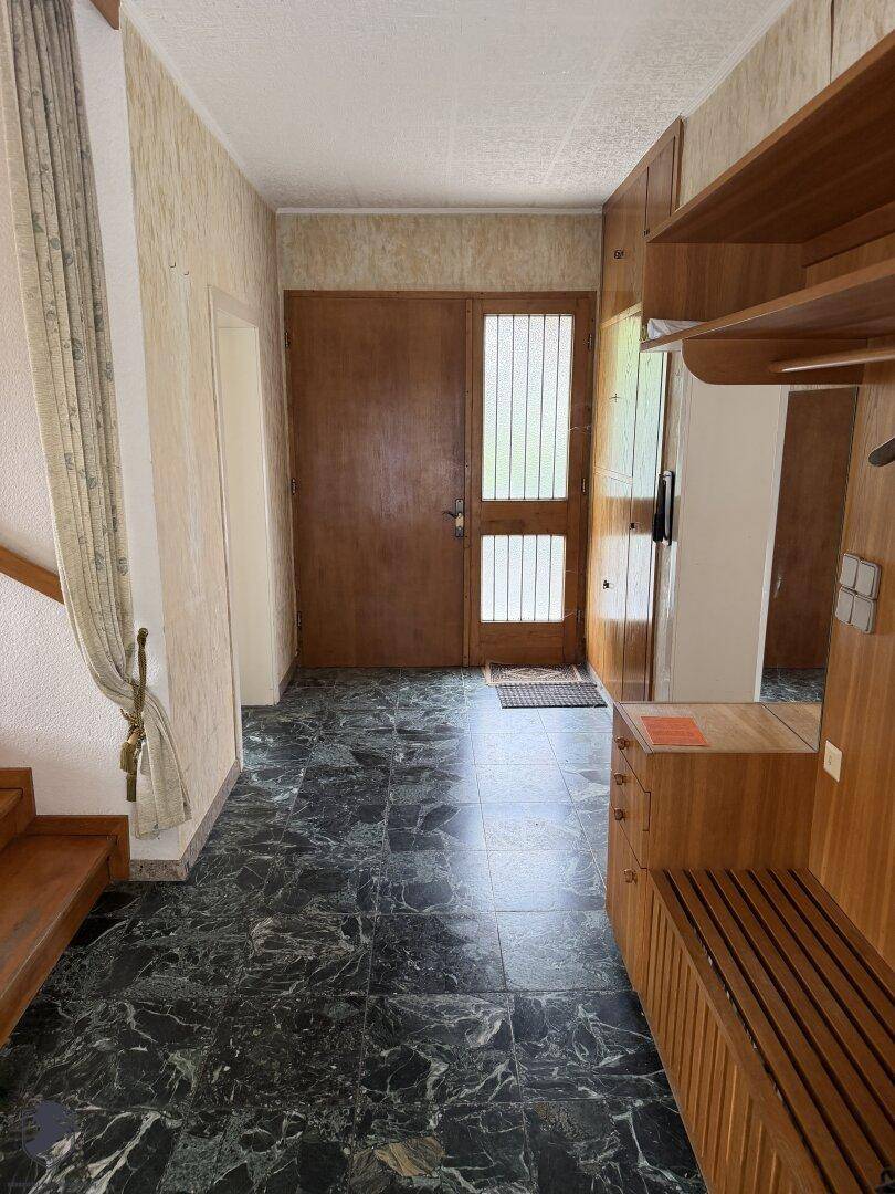 Eingangsbereich mit dunklem Fliesenboden, Holzmöbeln und einer Garderobe.