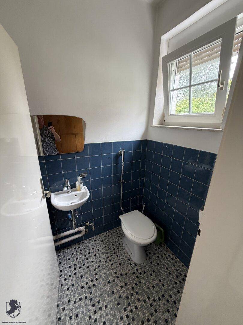Kleines Gäste-WC mit blauen Fliesen, Waschbecken und Fenster.