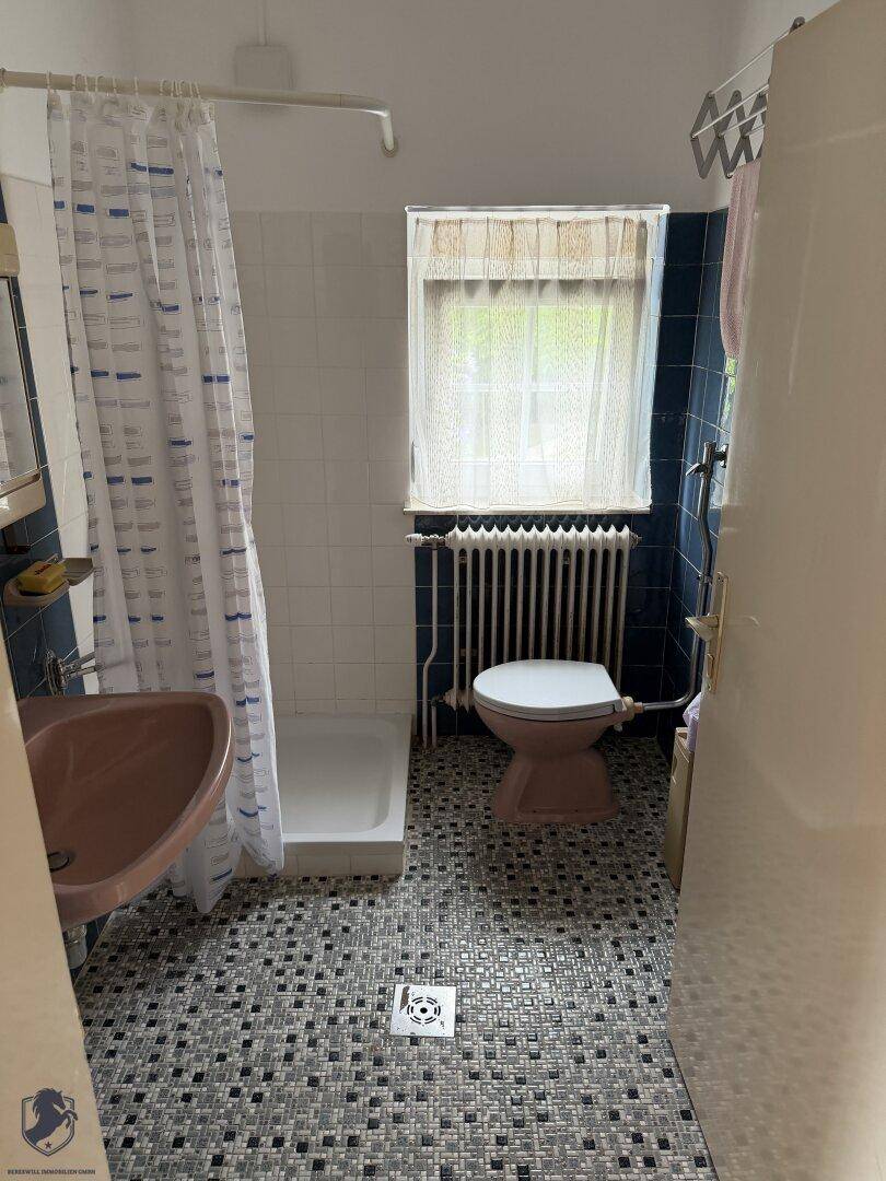 Badezimmer mit Dusche, rosa Waschbecken und WC, sowie einem Fenster.