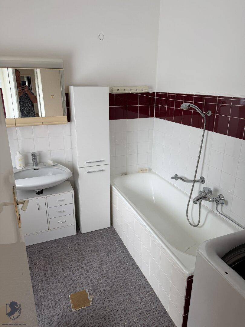 Badezimmer mit Badewanne, Waschbecken und roten Akzentfliesen.
