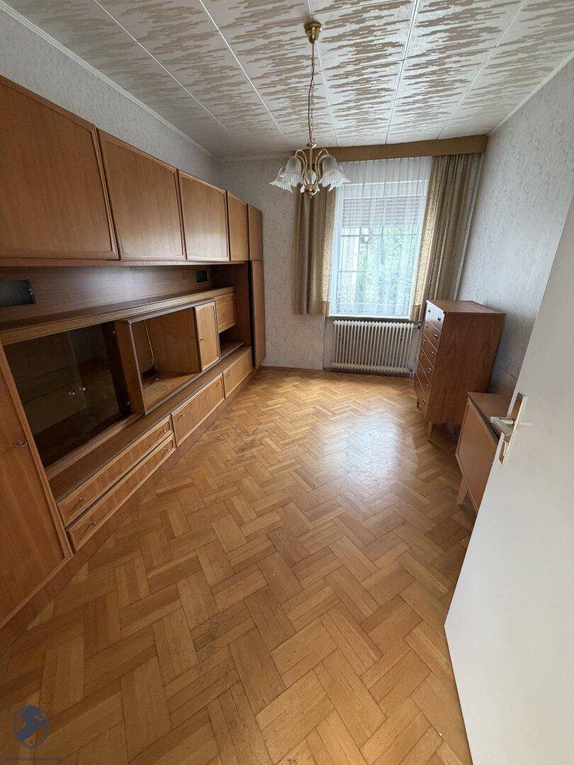 Schlafzimmer oder Arbeitszimmer mit Holzschrankwand, Parkettboden und Fenster.