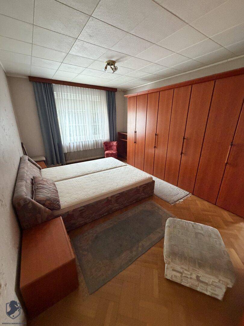 Schlafzimmer mit zwei Einzelbetten, Holzschrank und Parkettboden im 80er-Jahre-Stil.