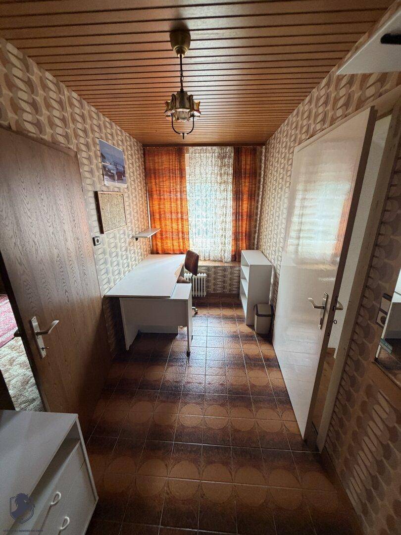Kleines Büro mit Schreibtisch, Regalen, gemusterten Tapeten und Holzdecke im Vintage-Stil.