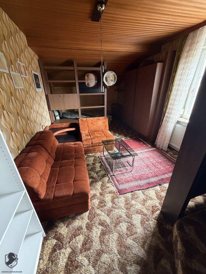 Gemütliches Wohnzimmer mit braunem Sofa, Teppichboden und Holzdecke im Retro-Stil.