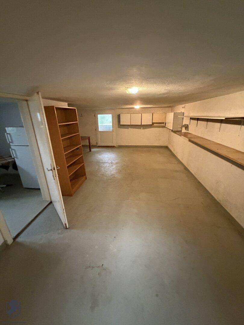 Großer Kellerraum mit Betonboden, Regalen und einem Kühlschrank für zusätzliche Lagerung.
