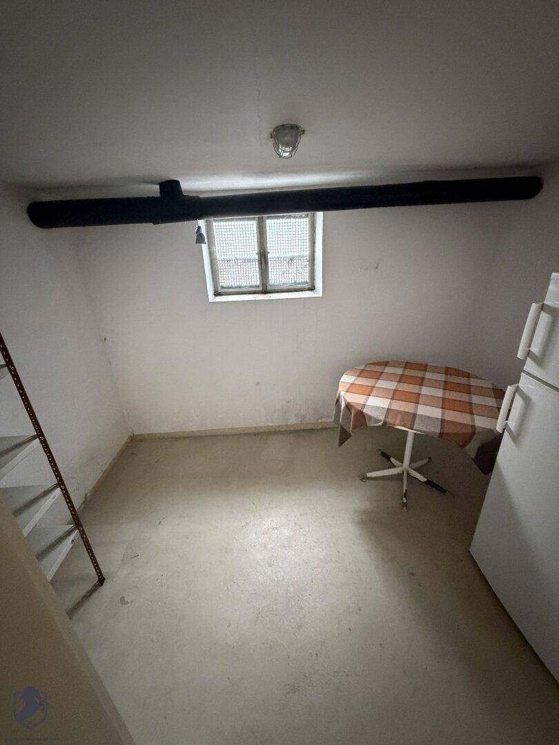 Kellerraum mit Betonboden, kleinem Fenster und einem Tisch mit karierter Decke.