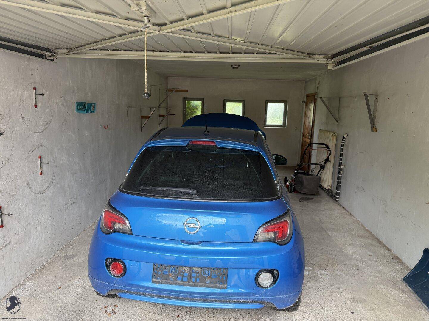 Garage mit einem blauen Auto, Betonboden und kleinen Fenstern für Tageslicht.
