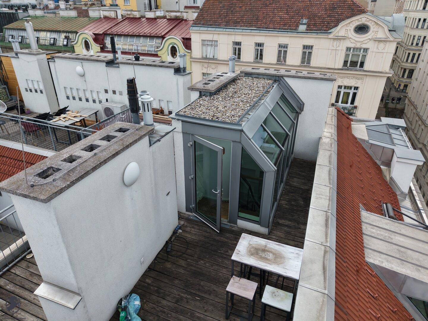 Dachterrasse mit Holzboden, modernem Glasaufbau und einem kleinen Tisch mit Stühlen für den Außenbereich.