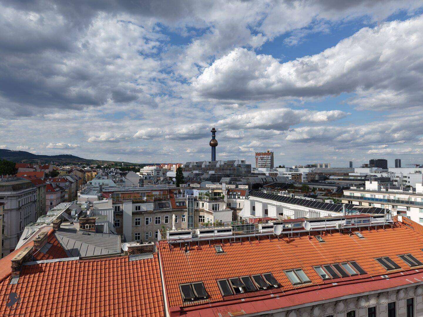 Panoramablick über die Stadt mit einer markanten Turmspitze am Horizont unter einem bewölkten Himmel.