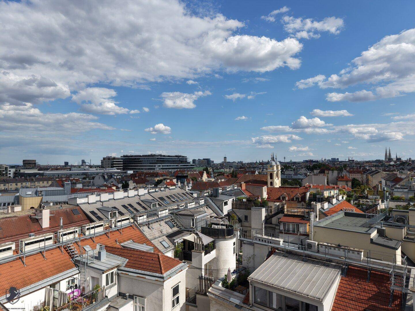 Heller Stadtblick mit historischen Gebäuden und einem Kirchturm, der sich über die Dächer erhebt.