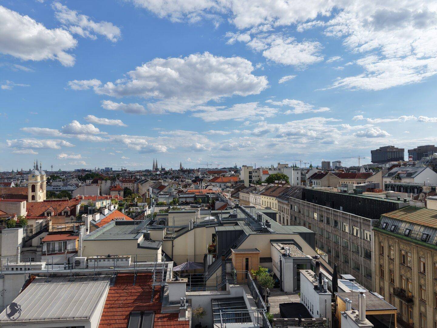 Klarer Panoramablick über die Stadt mit einer Vielzahl von Dächern und Gebäuden unter strahlend blauem Himmel.