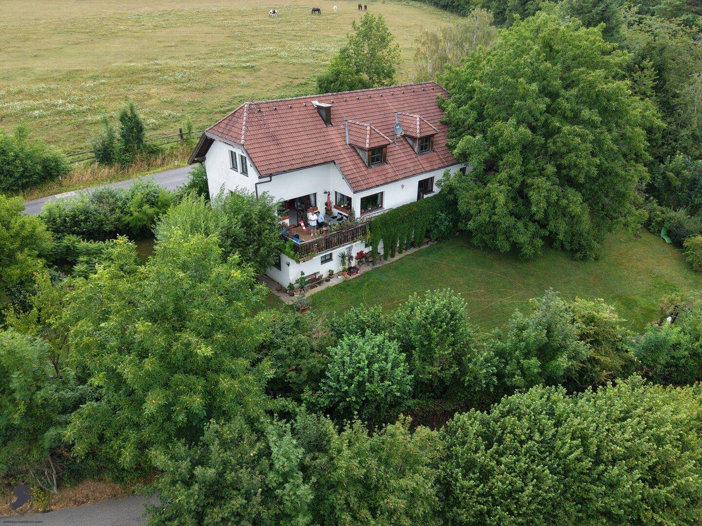 Nahaufnahme aus der Luft des Hauses mit Balkon, umgeben von üppigem Grün und weiten Feldern.