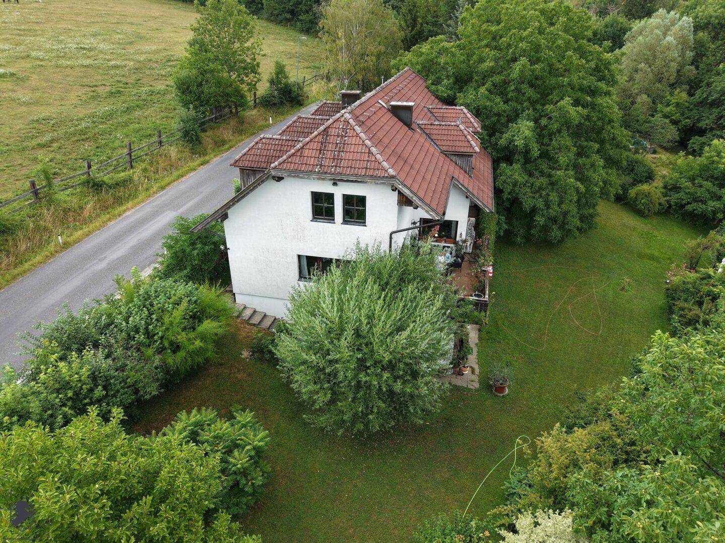Seitenansicht des Hauses aus der Luft, umgeben von einem gepflegten Garten und angrenzenden Feldern.