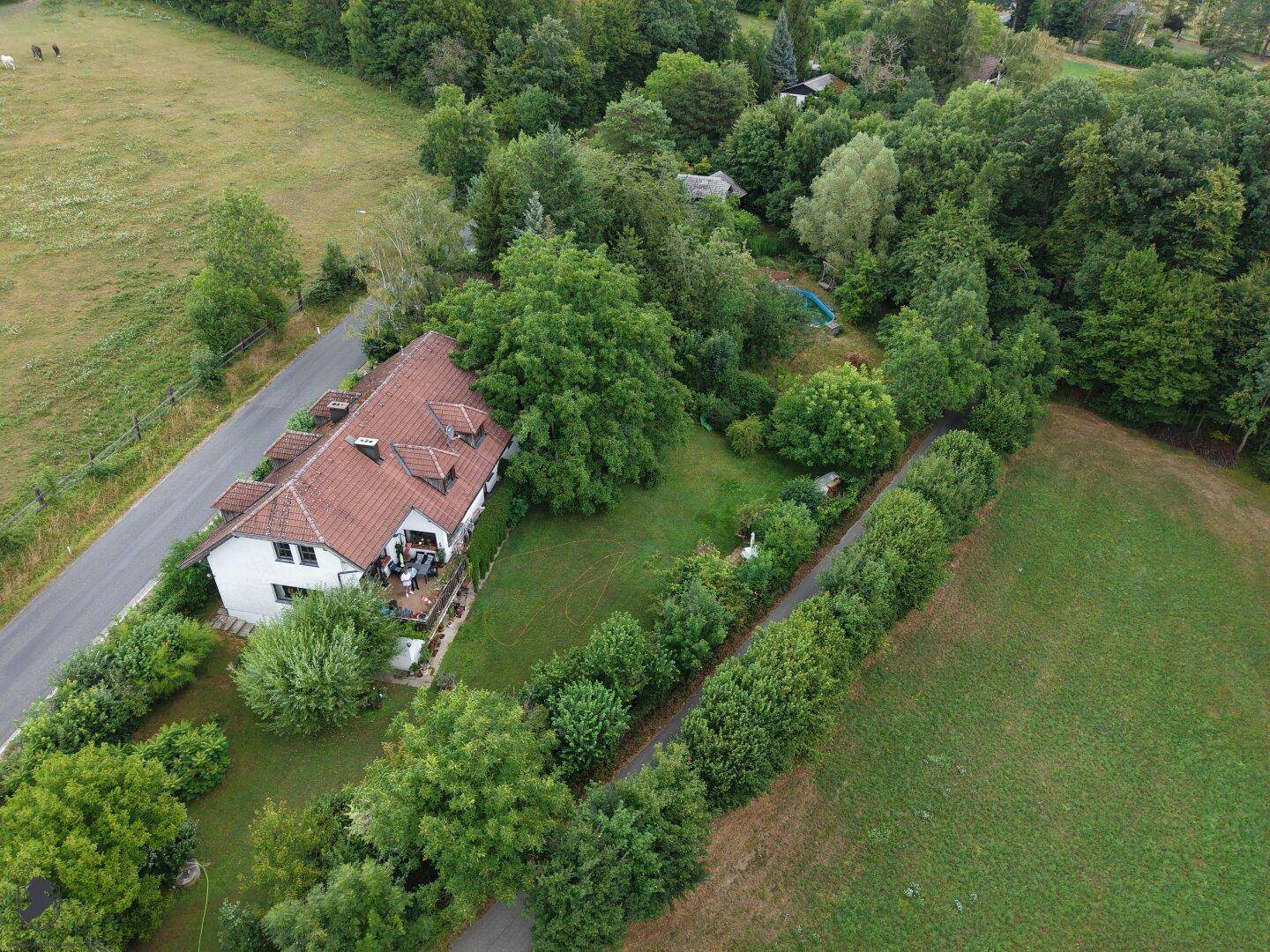 Luftaufnahme des Hauses mit Balkon, eingebettet in eine idyllische Landschaft mit Feldern und Wäldern.
