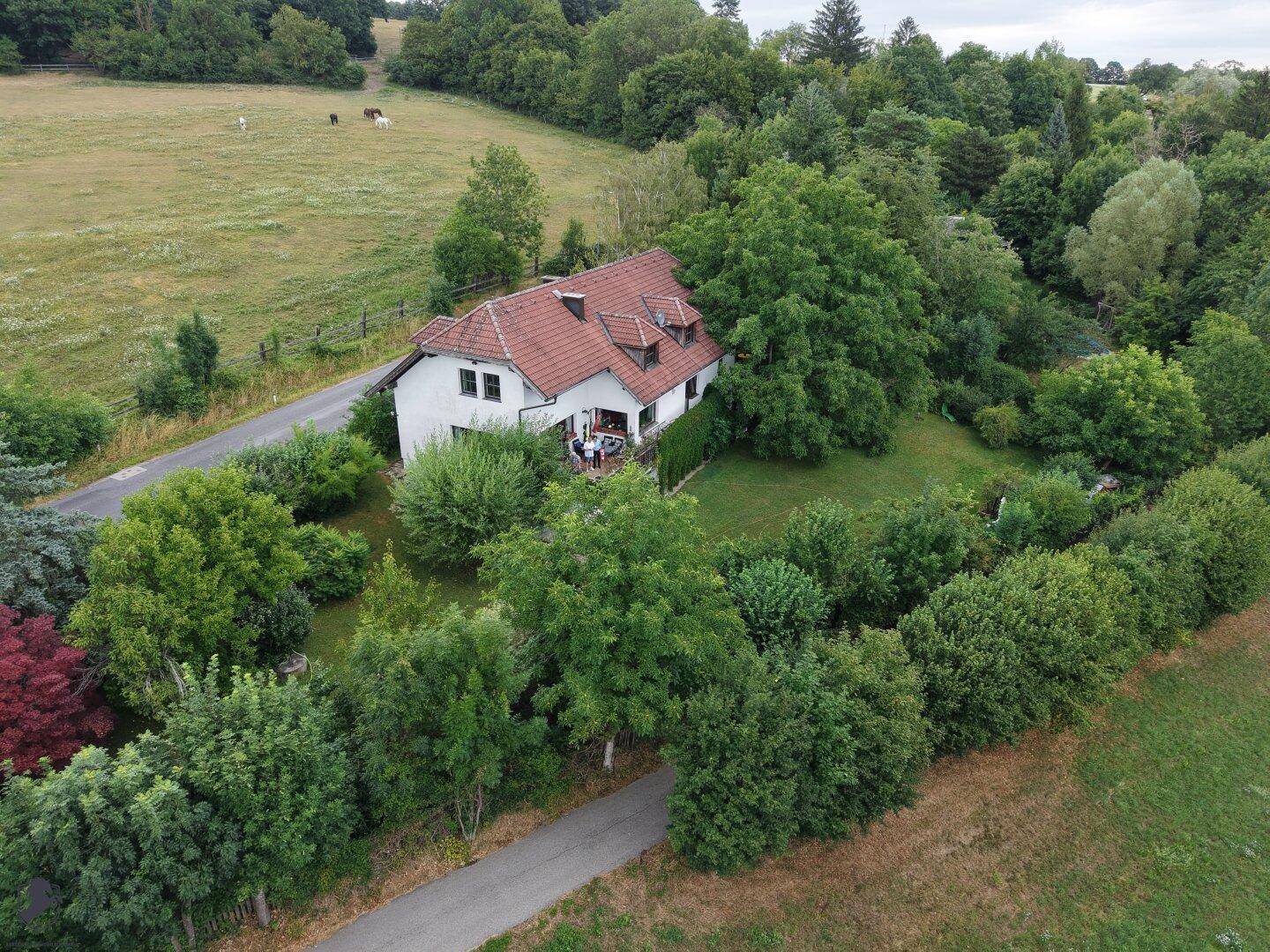 Luftaufnahme des Hauses mit Balkon, umgeben von üppiger Natur, Feldern und einem gepflegten Garten.