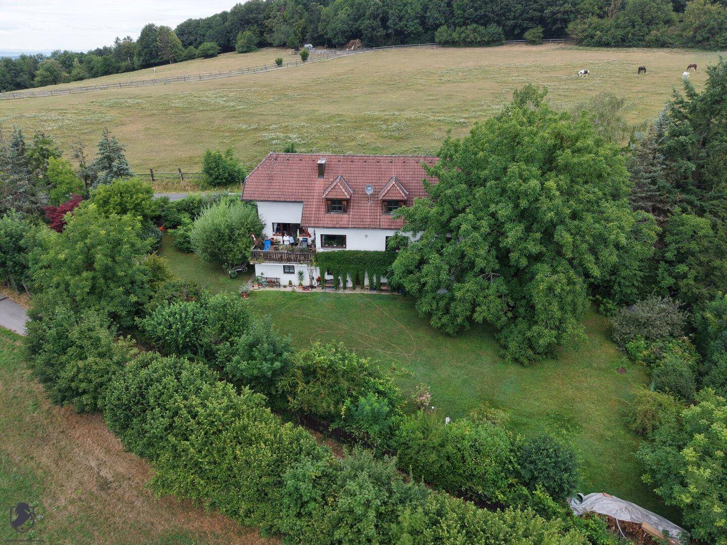 Detailreiche Luftaufnahme des Hauses mit Balkon, umgeben von einem großen Garten und ländlicher Umgebung.