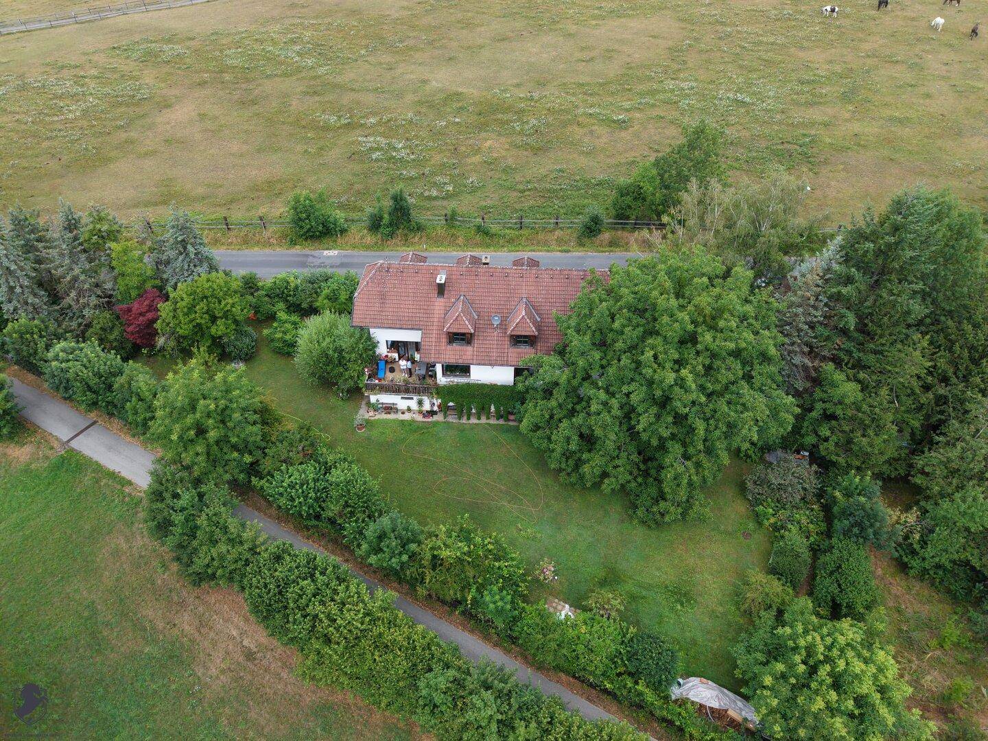 Weitläufige Luftaufnahme des Hauses mit Balkon, eingebettet in eine grüne Landschaft mit Feldern und Bäumen.
