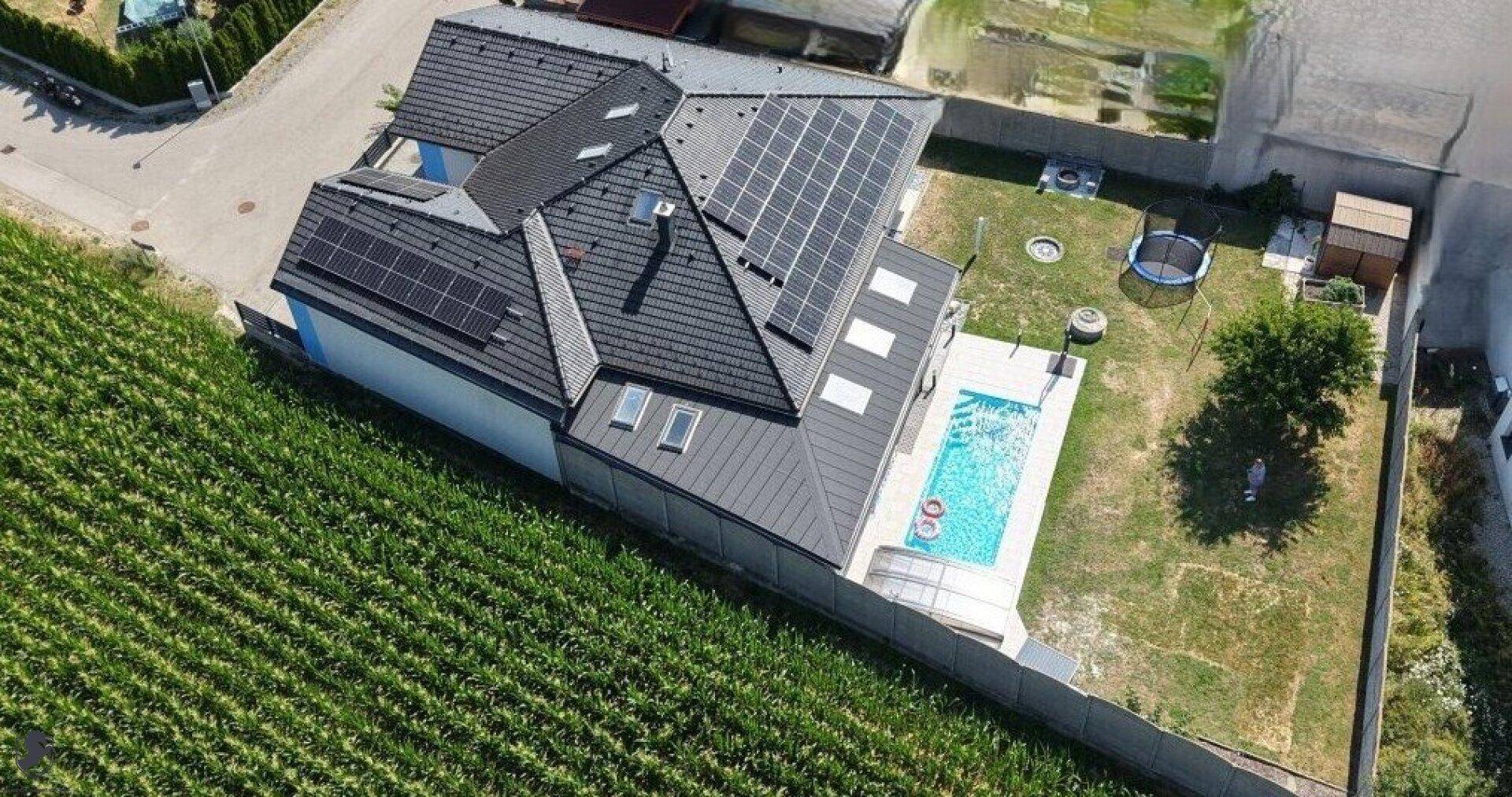 Luftaufnahme eines modernen Hauses mit Solaranlage, Pool und großem Garten, angrenzend an ein Feld.