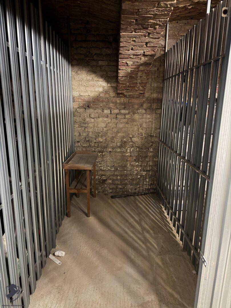 Kellerraum mit unverputzten Ziegelwänden, Betonboden und Metallabtrennungen für Lagerzwecke in einem Altbau.