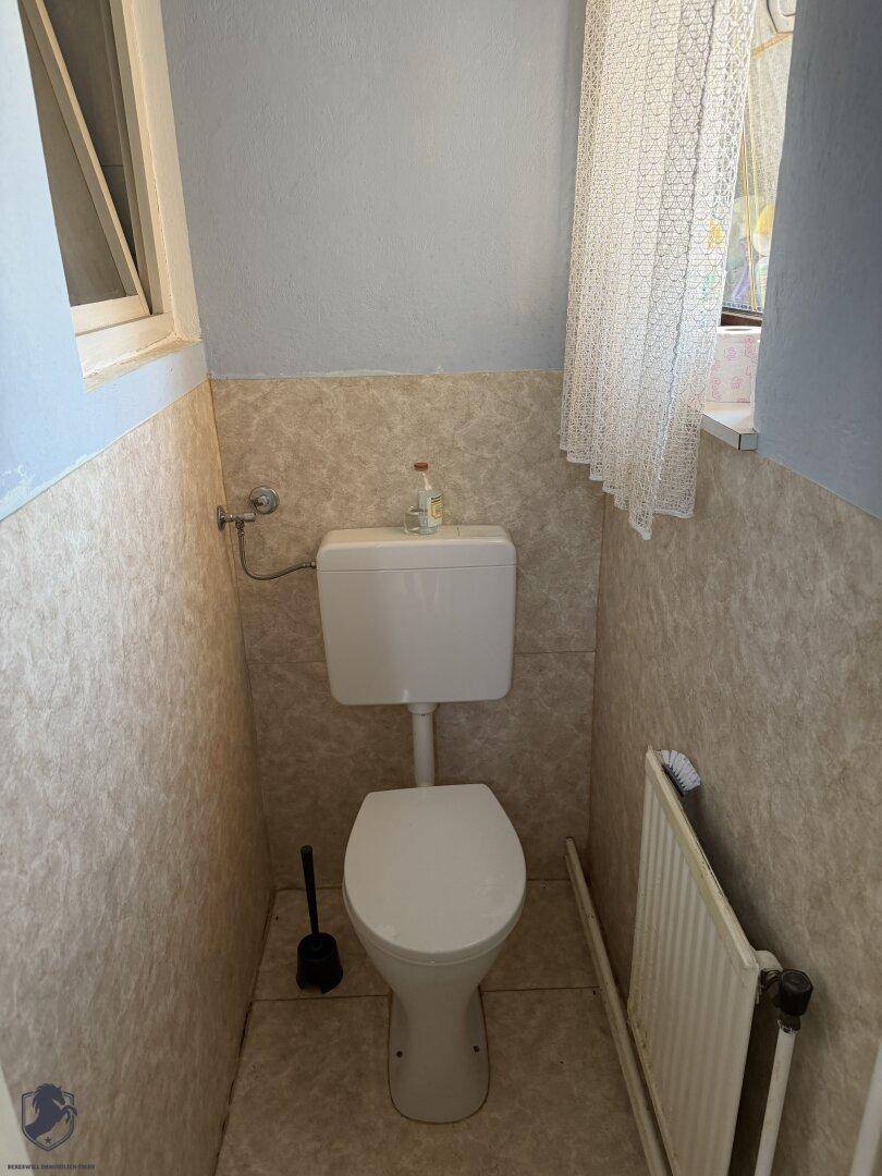 Kleines WC mit Fenster, Fliesen an den Wänden und einem Heizkörper.