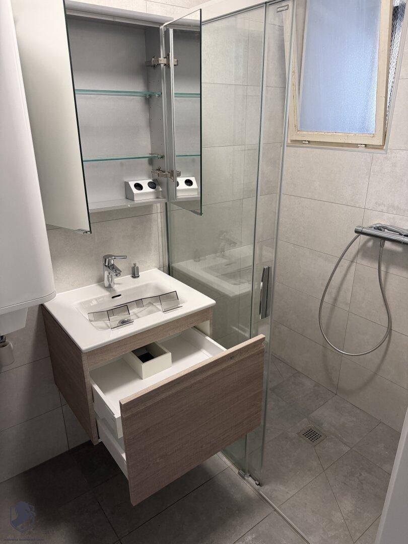 Modernisiertes Badezimmer mit Duschkabine, Waschtischunterschrank und Spiegelschrank.
