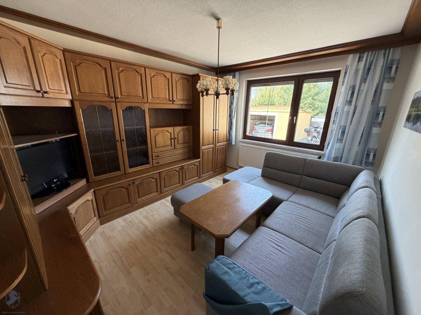 Gemütliches Wohnzimmer mit Holzschrankwand, Sofa und Blick ins Grüne.