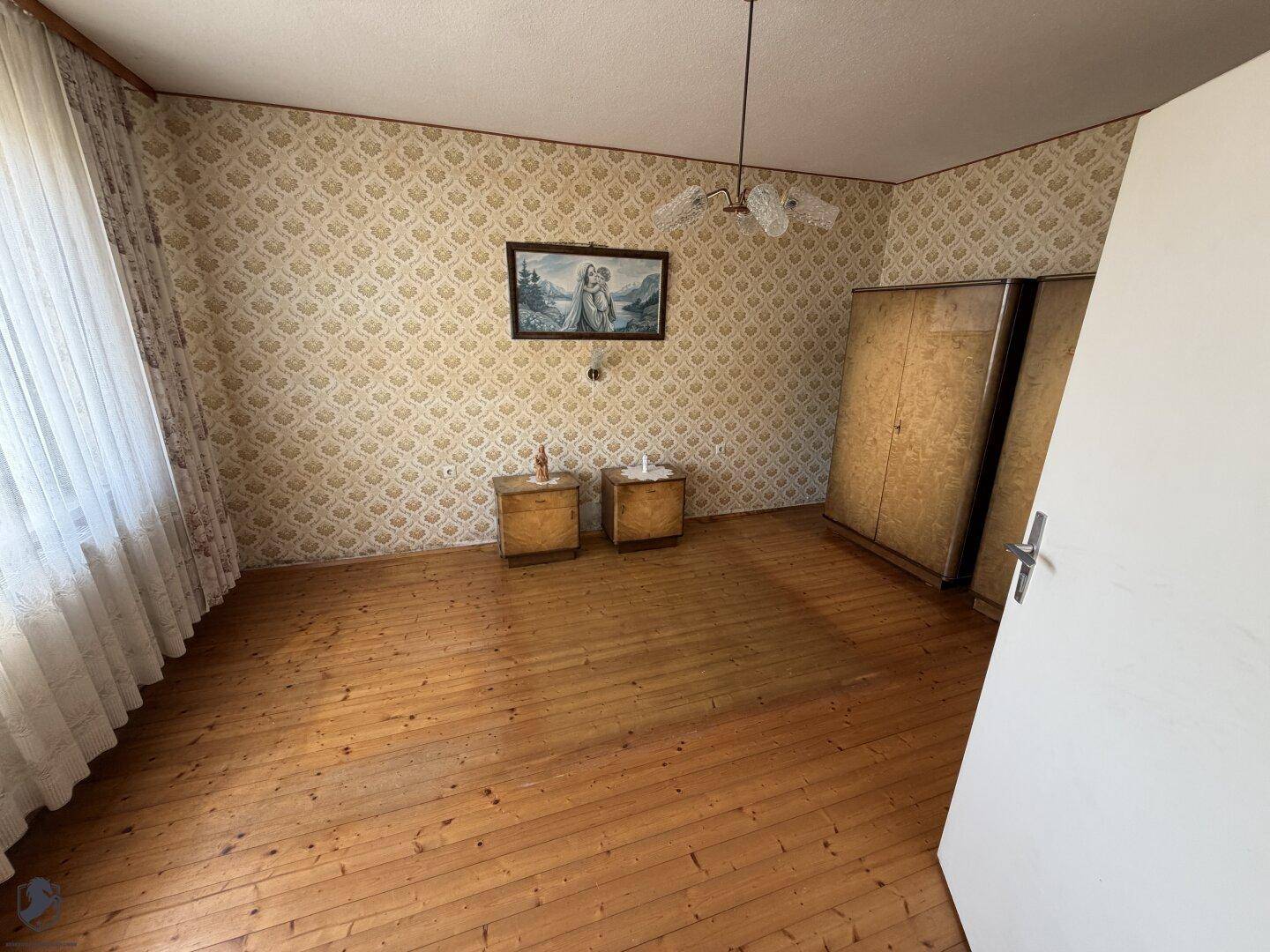 Leeres Schlafzimmer mit Holzdielenboden und gemusterter Tapete, bereit zur Renovierung.