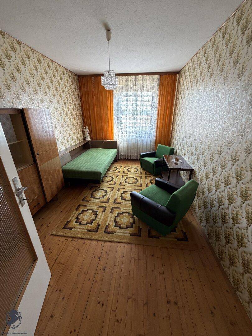Kleines Wohnzimmer mit Vintage-Möbeln, Holzdielenboden und gemusterter Tapete.