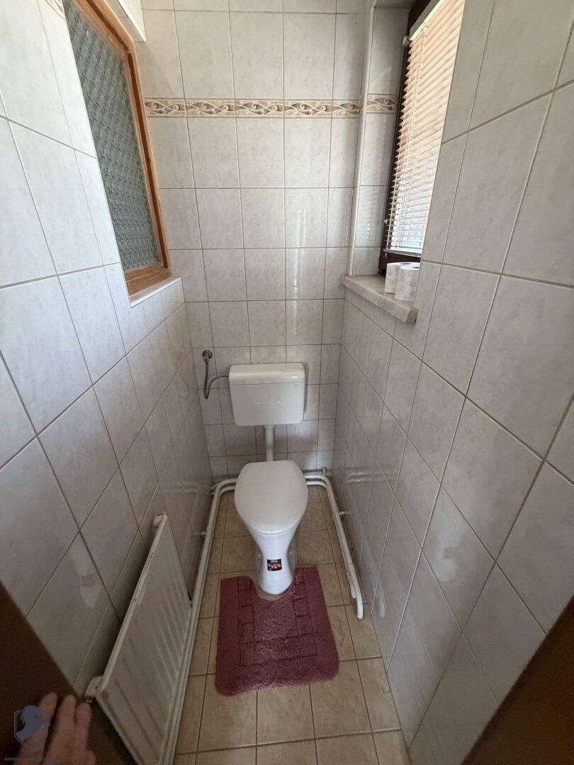 Gefliestes WC mit Fenster, Heizkörper und einfacher Ausstattung.