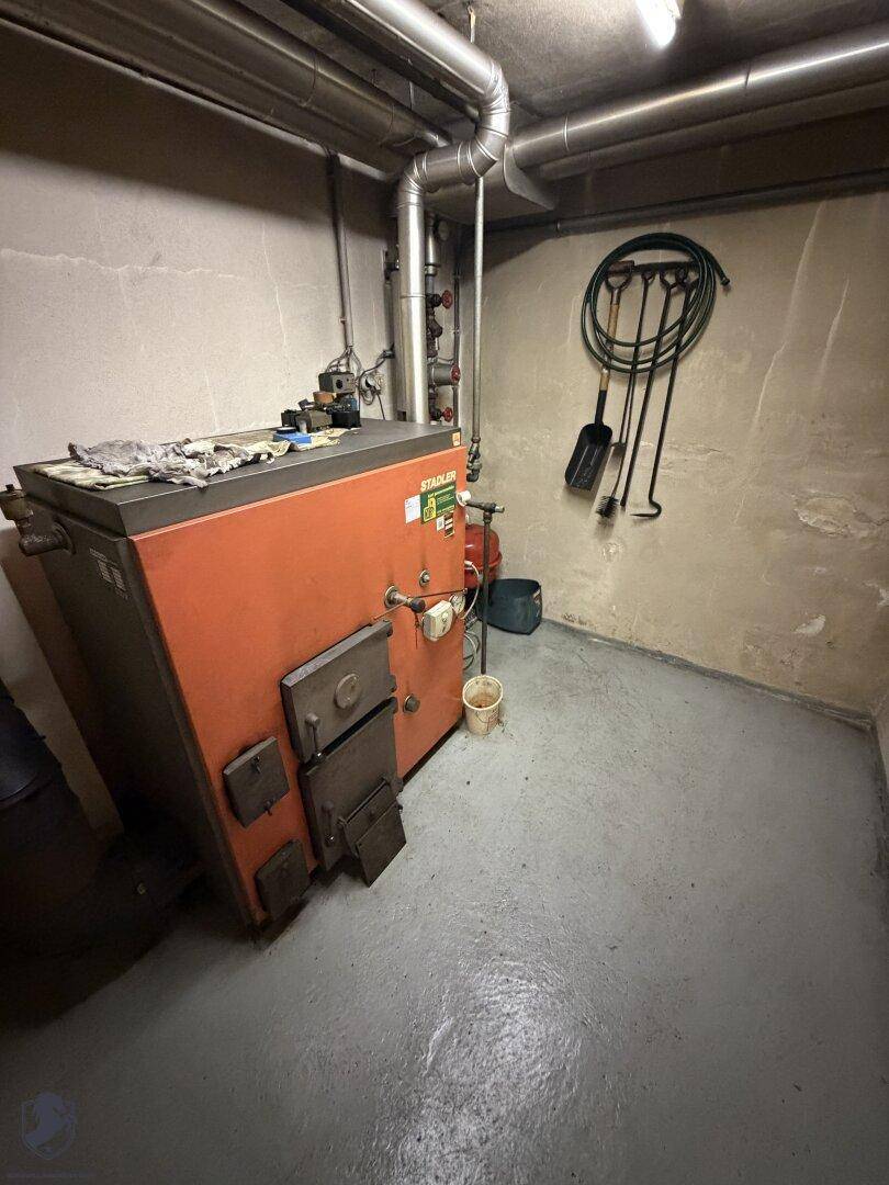 Heizraum im Keller mit großem Heizkessel, Rohren und Werkzeugen an der Wand.