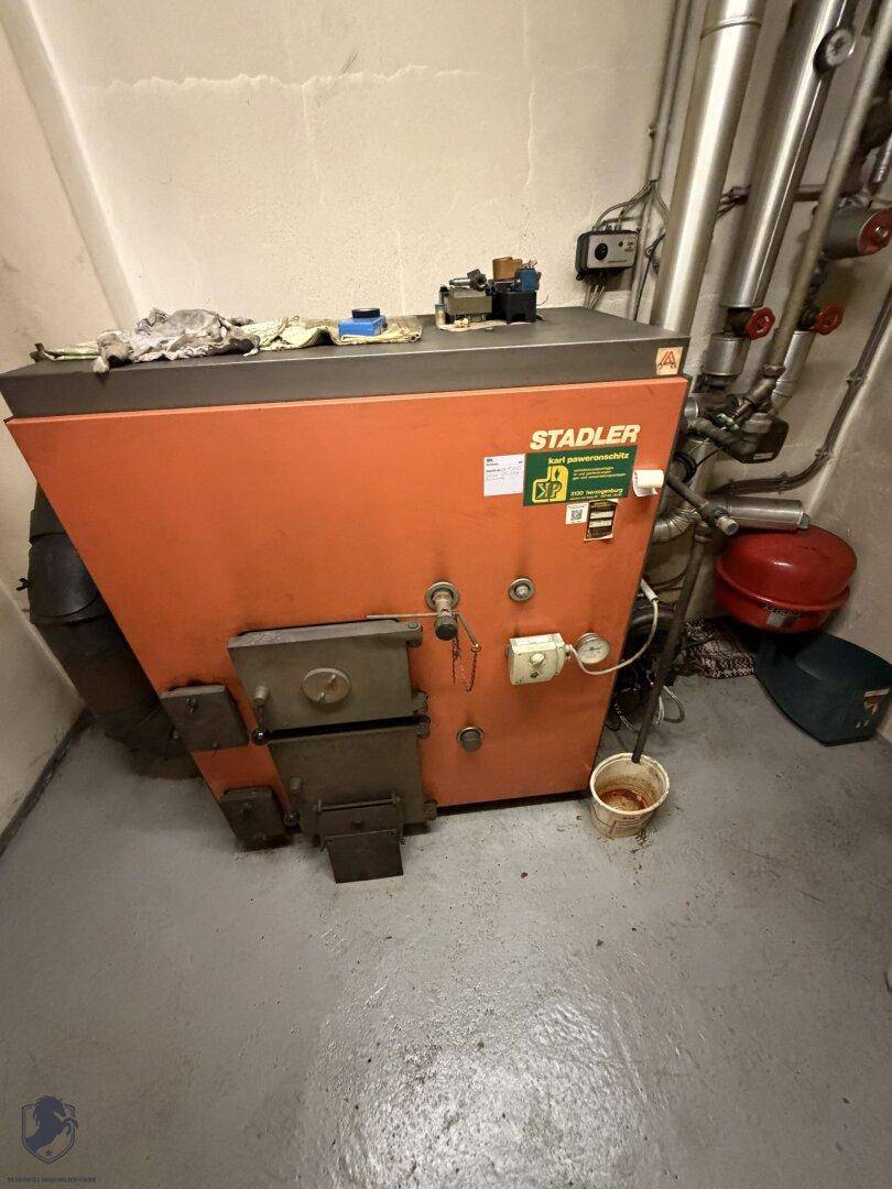 Nahaufnahme eines orangefarbenen Heizkessels der Marke Stadler in einem Kellerraum.