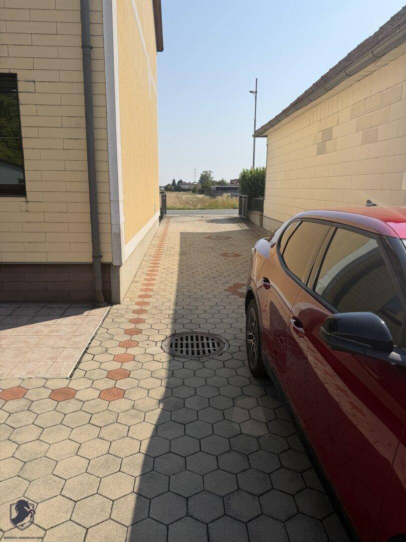 Gepflasterter Weg zwischen zwei Gebäuden mit einem geparkten roten Auto und Blick in die Ferne.