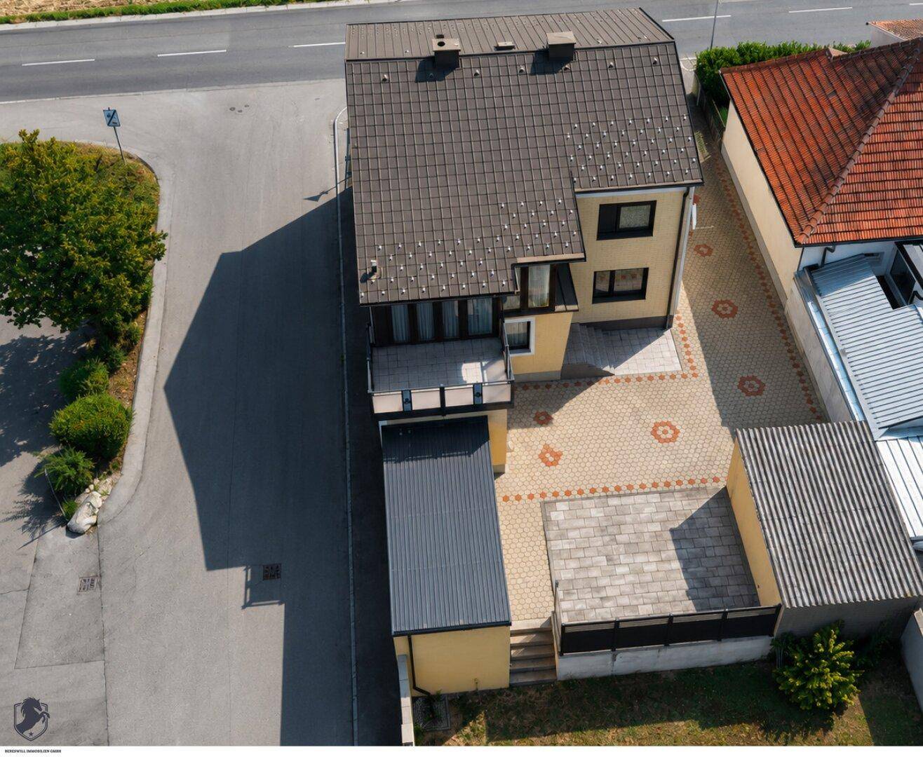 Luftaufnahme eines Einfamilienhauses mit gepflastertem Hof und angrenzender Straße.